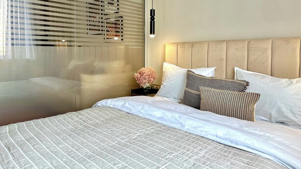 Une chambre d’hôtel avec un lit, une table de chevet, un vase avec des fleurs et une fenêtre avec des stores.