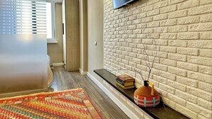 Un salon moderne avec un mur en briques, un téléviseur fixé au mur, une porte en bois et un tapis à motifs.