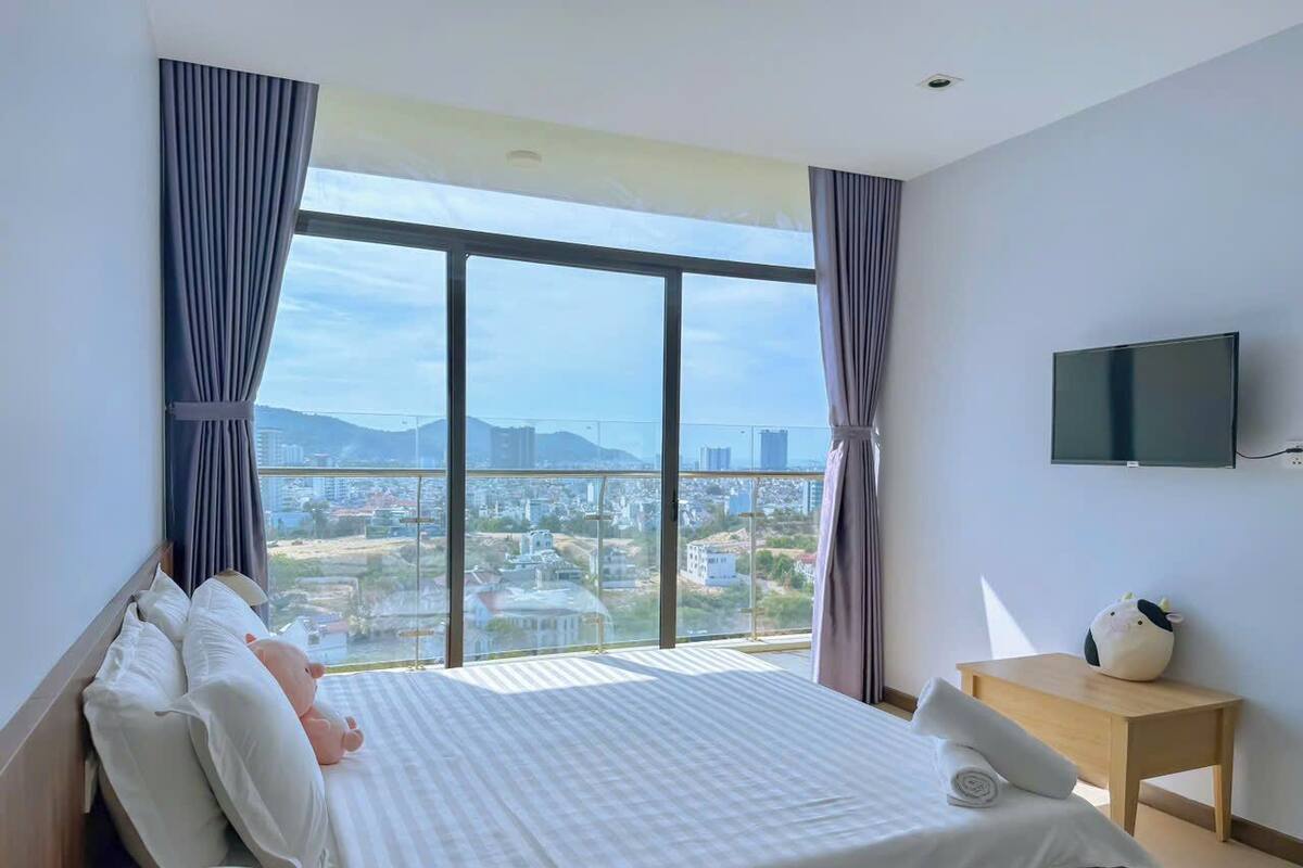 A hotel room with a large bed, a TV, a small table, and a view of the city.