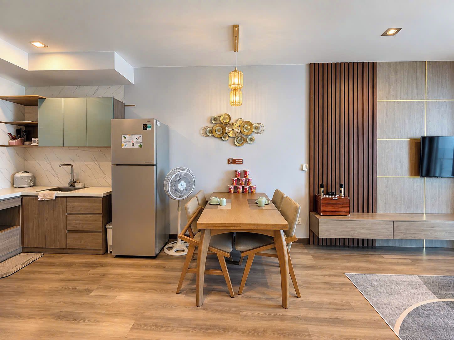 A modern kitchen with a built-in refrigerator, a dining area with a wooden table and chairs, and a wall-mounted TV.