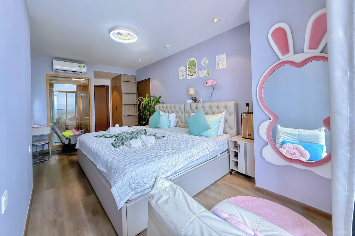 A bedroom with a large bed, bedside tables, a vanity, and a mirror with a bunny design.