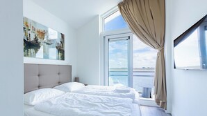 Ein modernes Hotelzimmer mit einem großen Bett, Meerblick und einem Bild an der Wand.