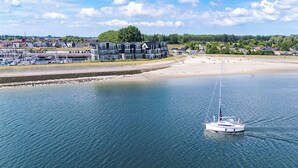 Eine Küstenlandschaft mit einem Yachthafen, einem Sandstrand und einer Reihe mehrstöckiger Gebäude.