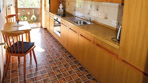 Una cucina compatta con mobili in legno, pavimento piastrellato e zona pranzo con sedia e tavolo.