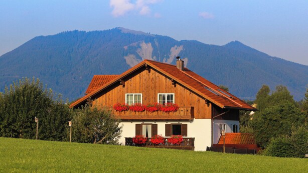 Una casa di legno con tetto spiovente, immersa in un prato erboso e alberi, con montagne sullo sfondo.