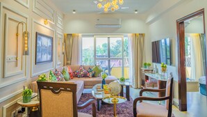 A well-lit living room with a sofa, chairs, a coffee table, and a TV. - Alaya Stays Veera Marina 2BHK (Candolim)