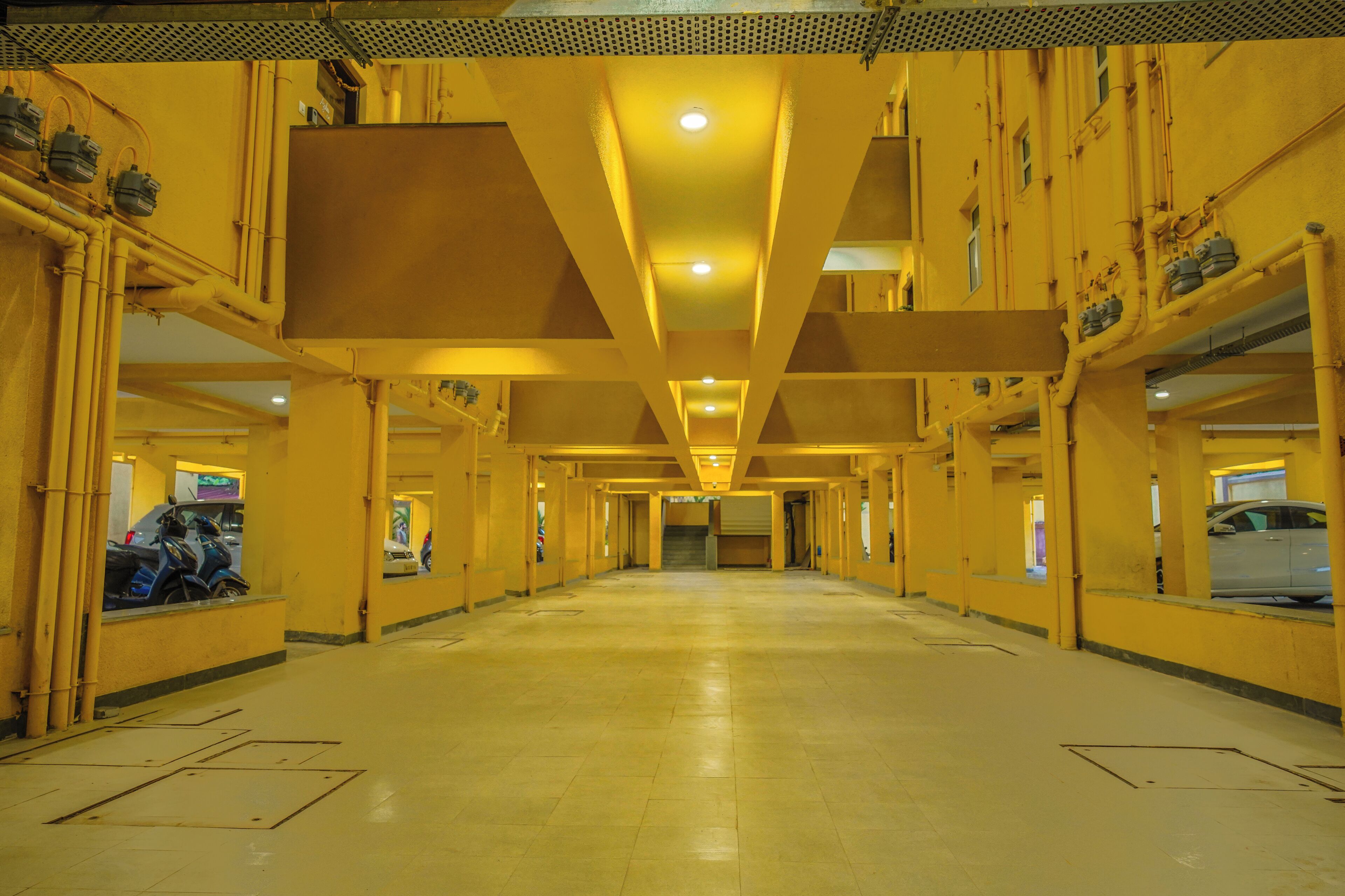 A long, empty corridor with yellow walls and ceiling, lined with windows and doors, and equipped with overhead lighting.
