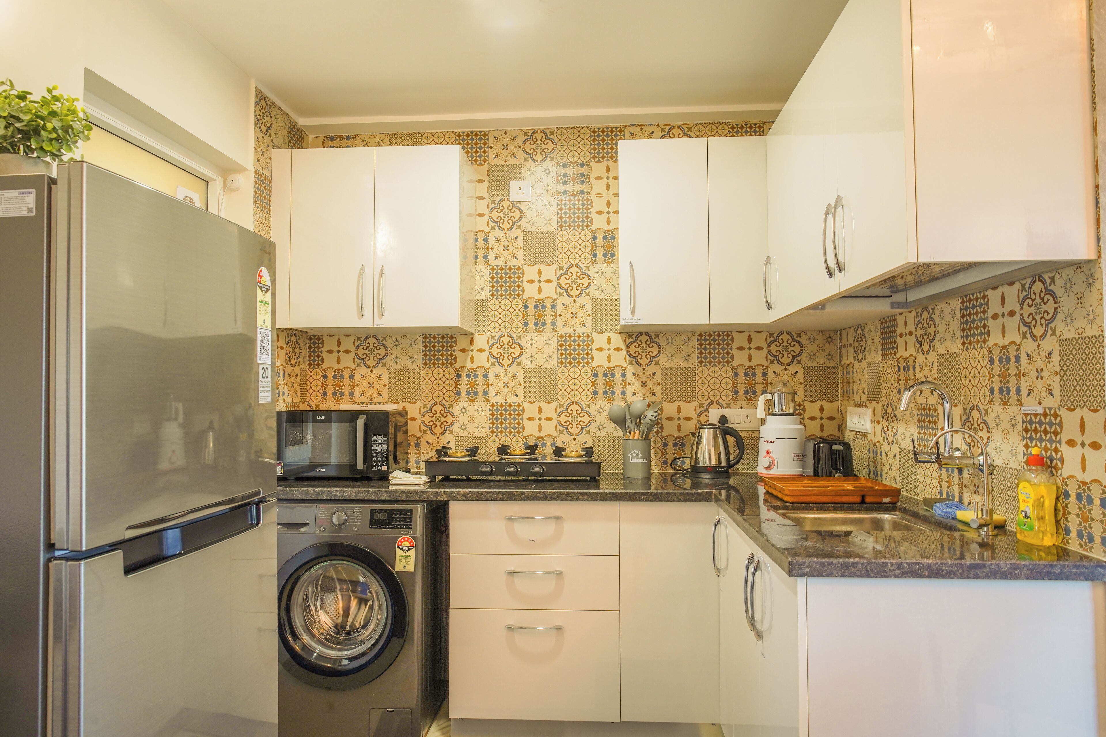 A compact kitchen with a stainless steel refrigerator, a washing machine, a microwave, and a stove.
