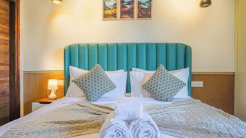 A neatly made bed with a teal headboard, two patterned pillows, and rolled towels on the bed.