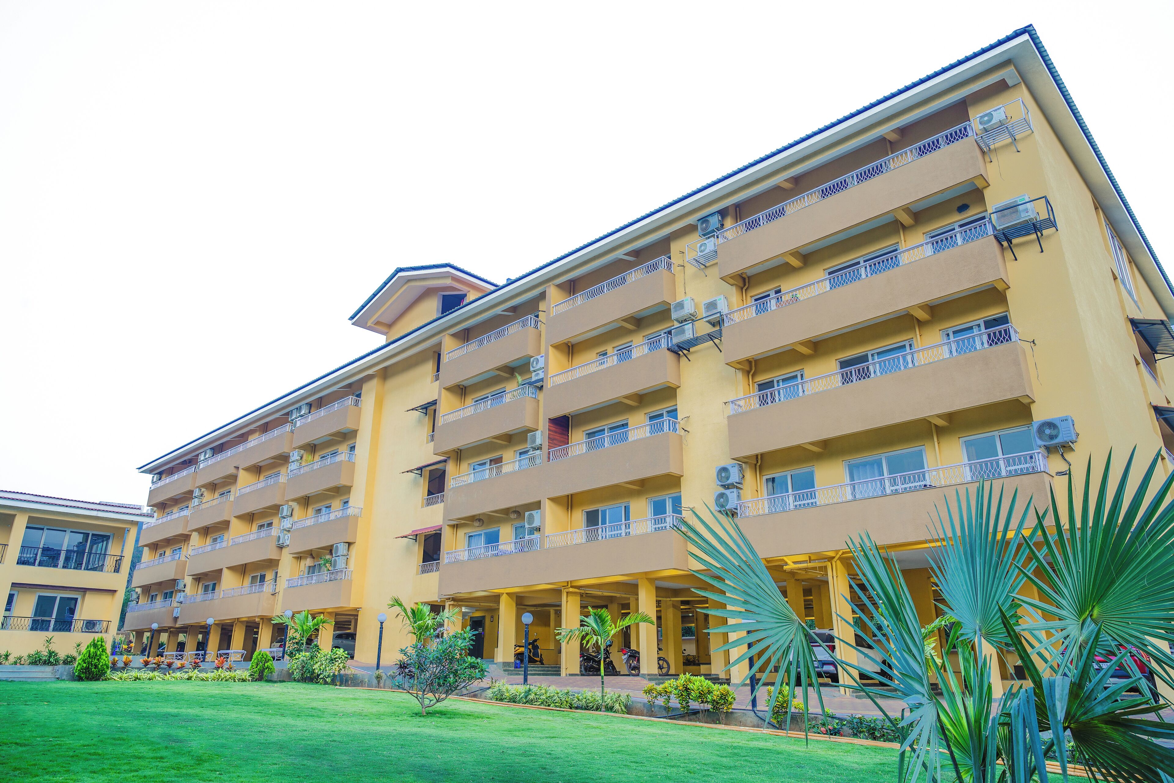 Un hotel de varios pisos con balcones, unidades de aire acondicionado y un césped bien cuidado con palmeras.