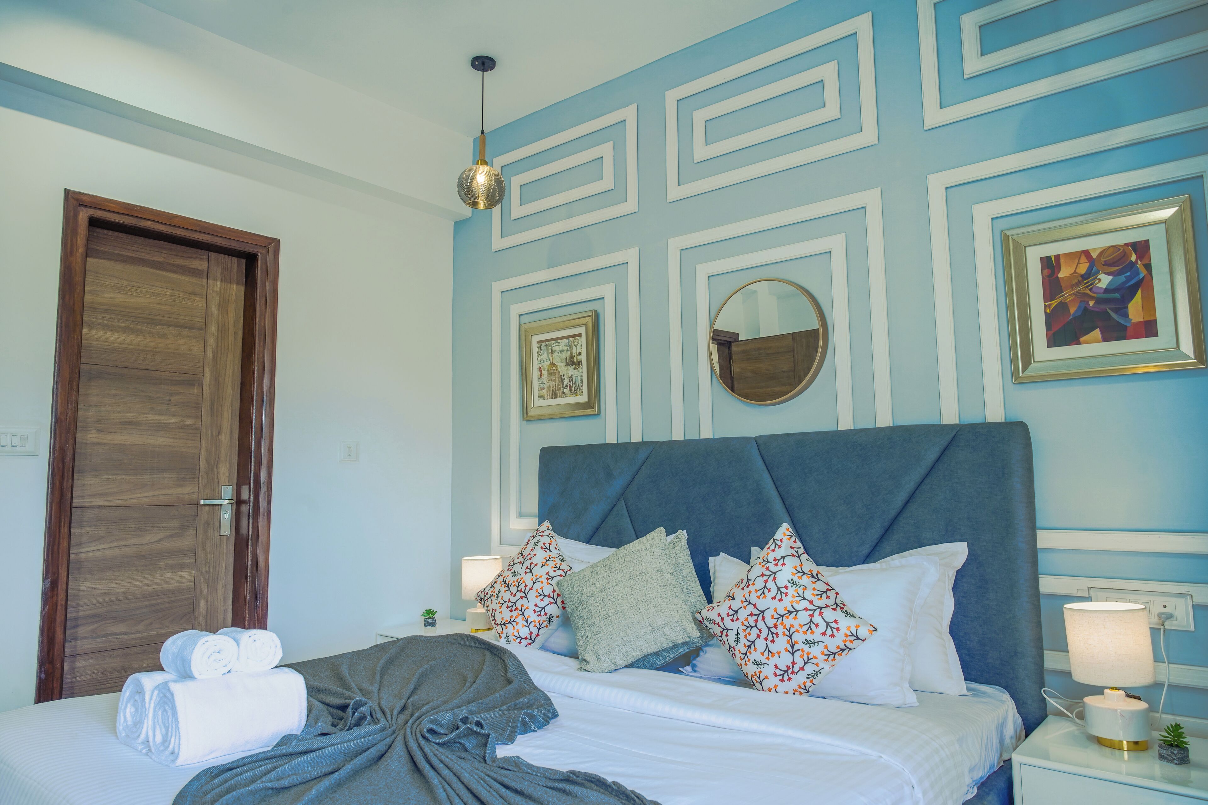 A neatly made bed with pillows and a blanket, a wooden door, a wall with decorative molding, and a framed picture.