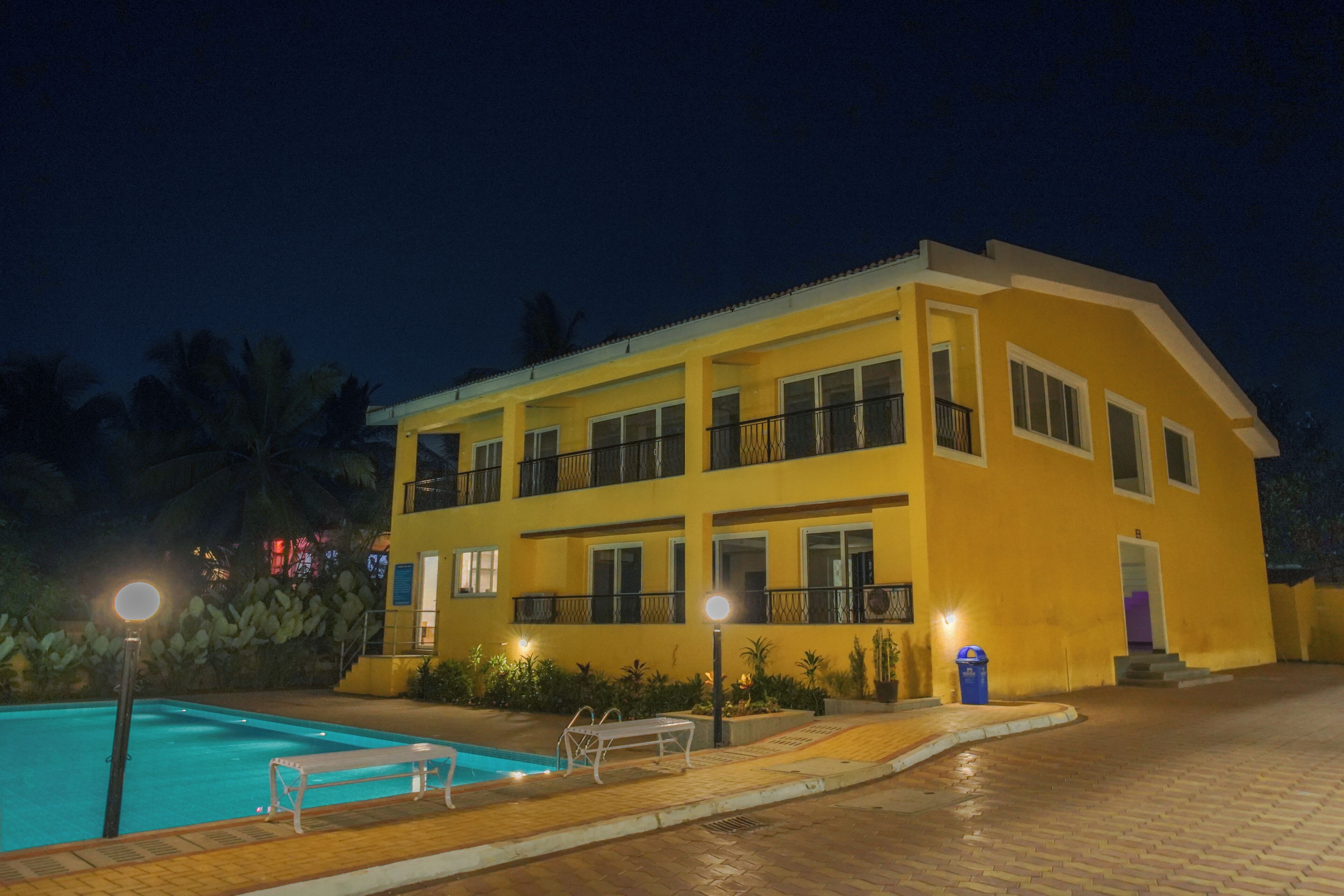 A two-story hotel with a swimming pool, outdoor seating, and a well-lit entrance.