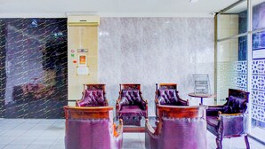 Un hall d’entrée avec quatre fauteuils violets, un mur en marbre et une cloison en verre.