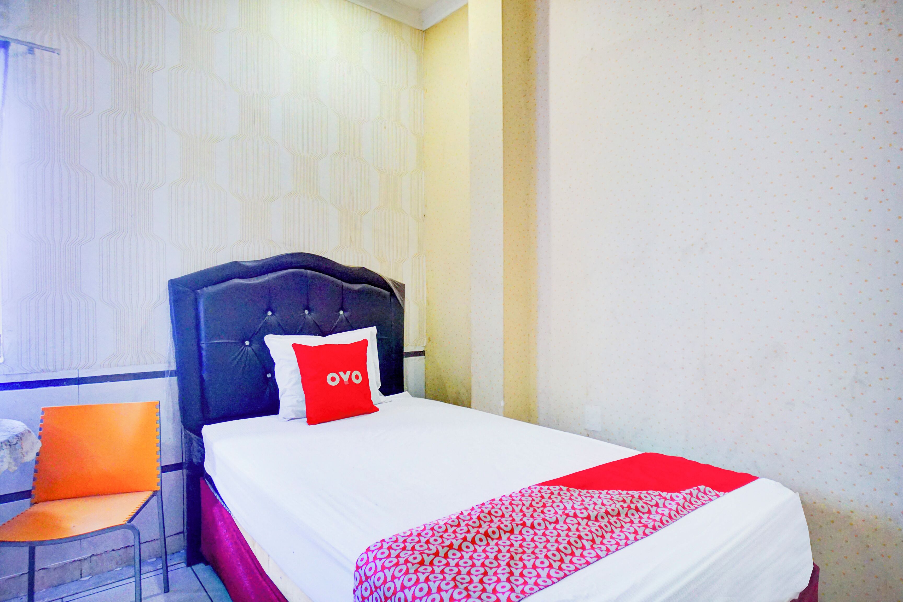 A hotel room with a bed, a chair, and a window with patterned curtains.