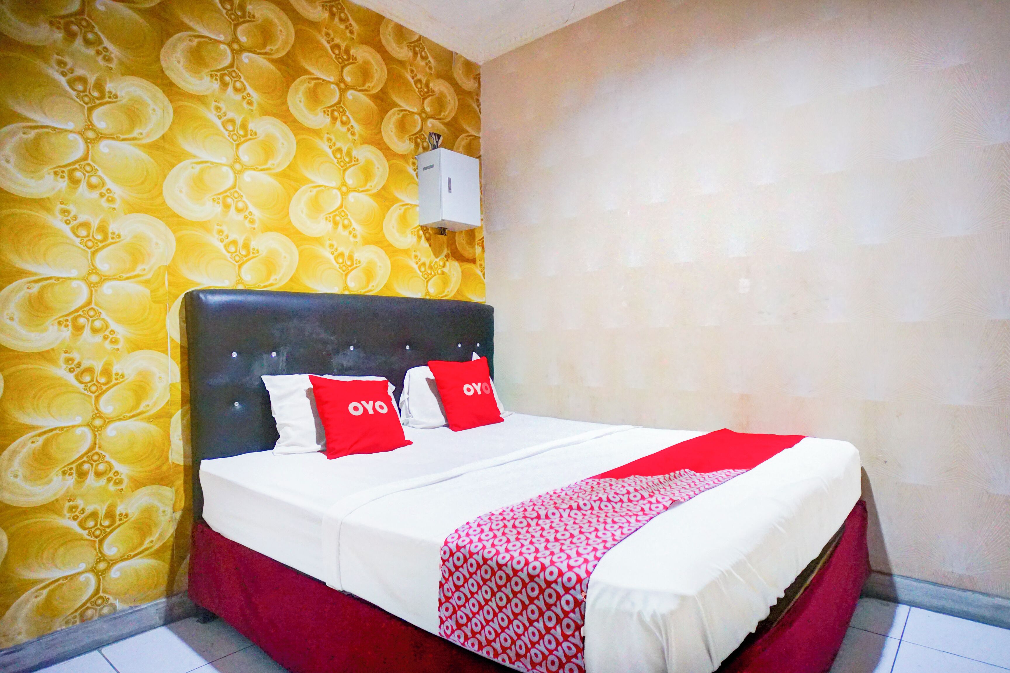 A neatly made bed with a red and white patterned bedspread, a black headboard, and two red pillows with "OYO" branding.