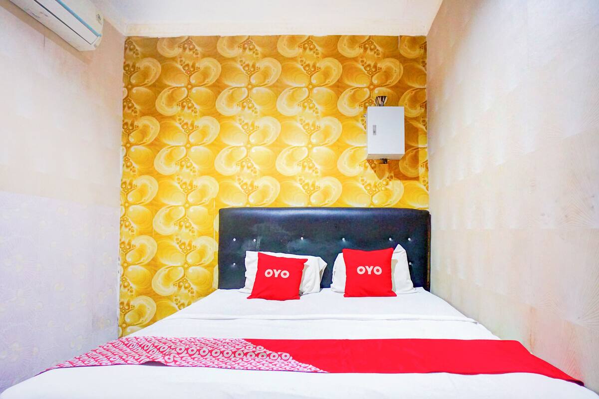 Hotelkamer met een bed, twee rode kussens met 'OYO'-logo, een witte airconditioning en een behang met een geel patroon.