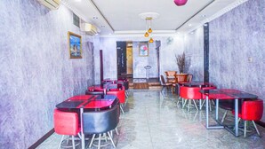 Un hall d’hôtel aux murs de marbre, aux tables rouges et noires, et doté d’un ventilateur de plafond.