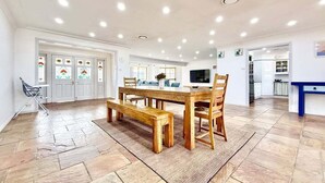 A spacious dining area with a wooden table and benches, a television, and a kitchen area in the background.