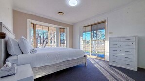 A bedroom with a bed, a desk, a dresser, and large windows.