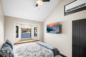 A bedroom with a bed, a window with a view, a ceiling fan, and an air conditioning unit.