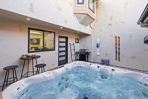 A hot tub in a backyard with a table and chairs, a ladder, and skis on the wall.