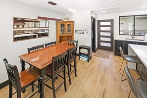Un comedor con mesa y sillas de madera, un armario con puertas de vidrio y una zona de cocina con lavamanos y encimera.