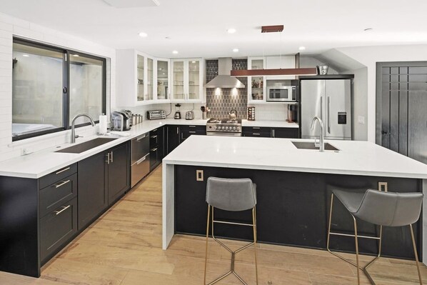 Una cocina moderna con una isla grande, muebles oscuros y electrodomésticos de acero inoxidable.