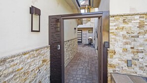 Un estrecho pasillo con una puerta metálica que da a una habitación con pared de piedra y un banco.