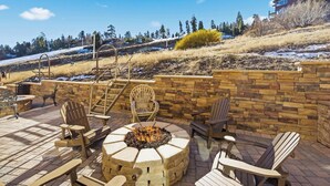 An outdoor patio with a stone fire pit, wooden chairs, and a stone wall.
