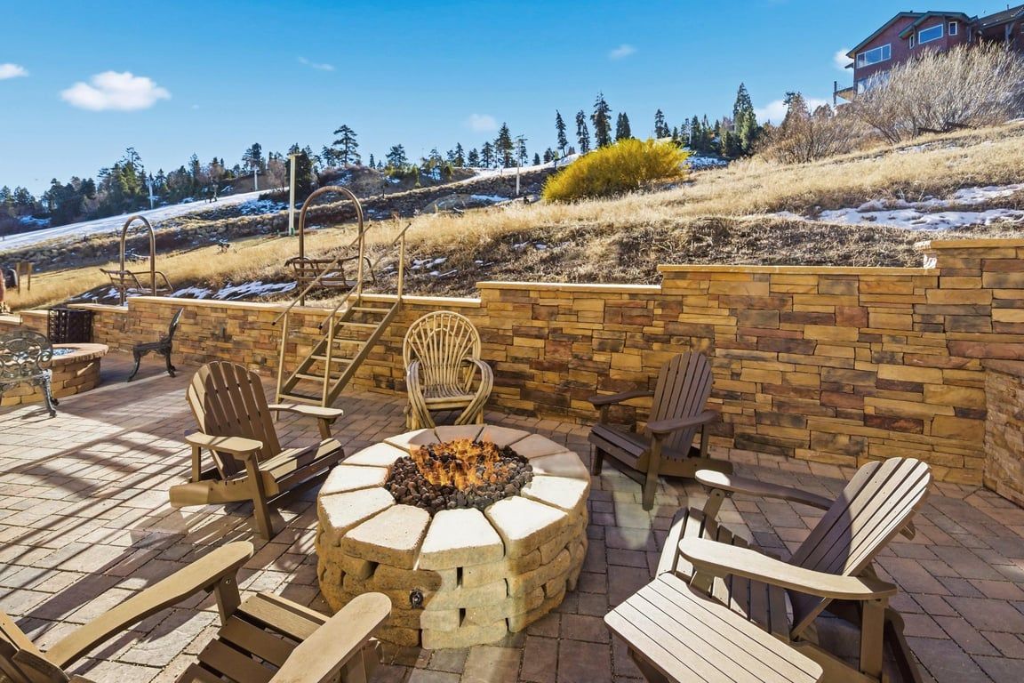 A patio with Adirondack chairs, a fire pit, and a stone wall.