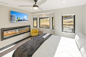 Un dormitorio moderno con una cama grande, un ventilador de techo, un televisor montado y una chimenea.