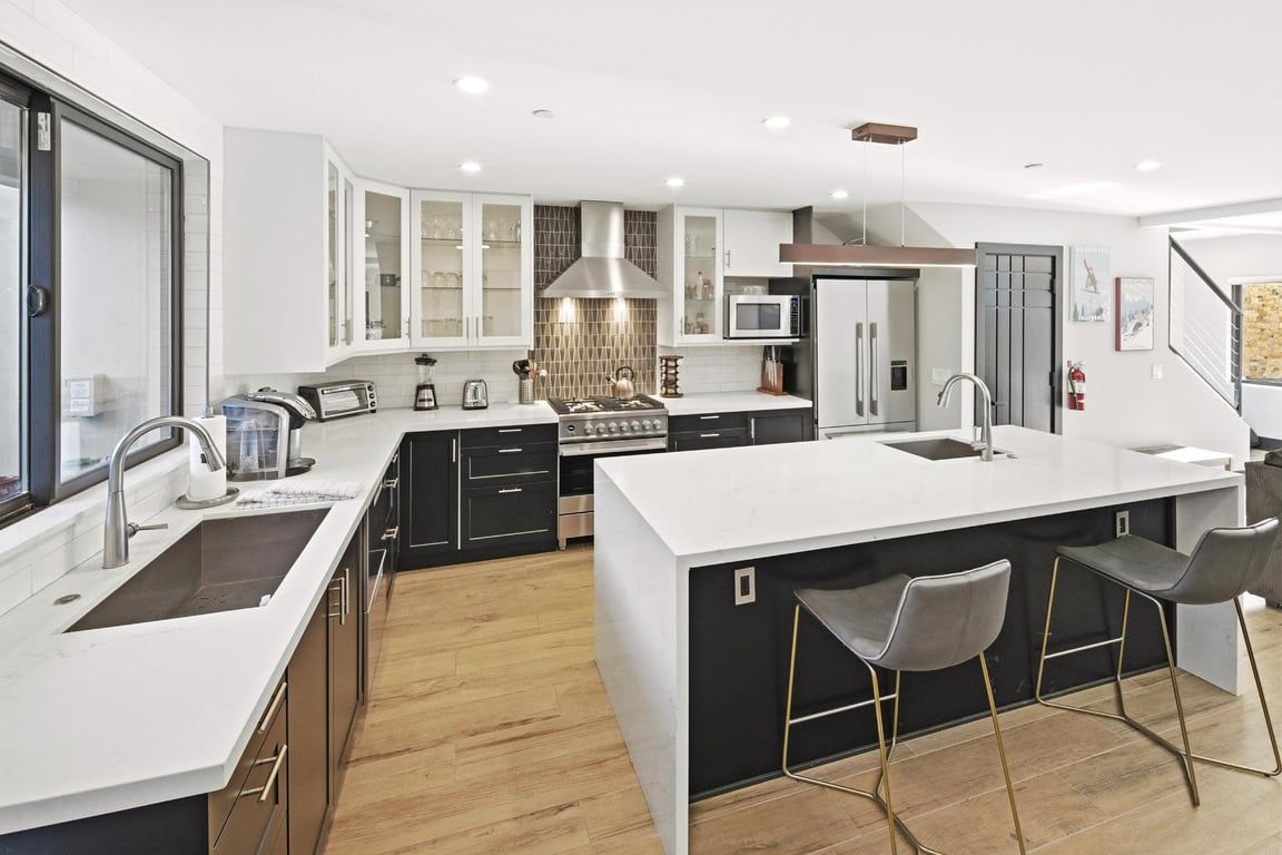 A modern kitchen with a central island, bar stools, and a microwave.