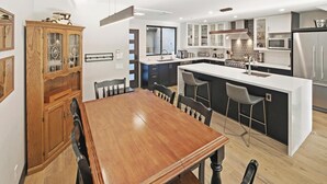 Una cocina moderna con una isla central, armarios oscuros y una mesa de comedor de madera con sillas.