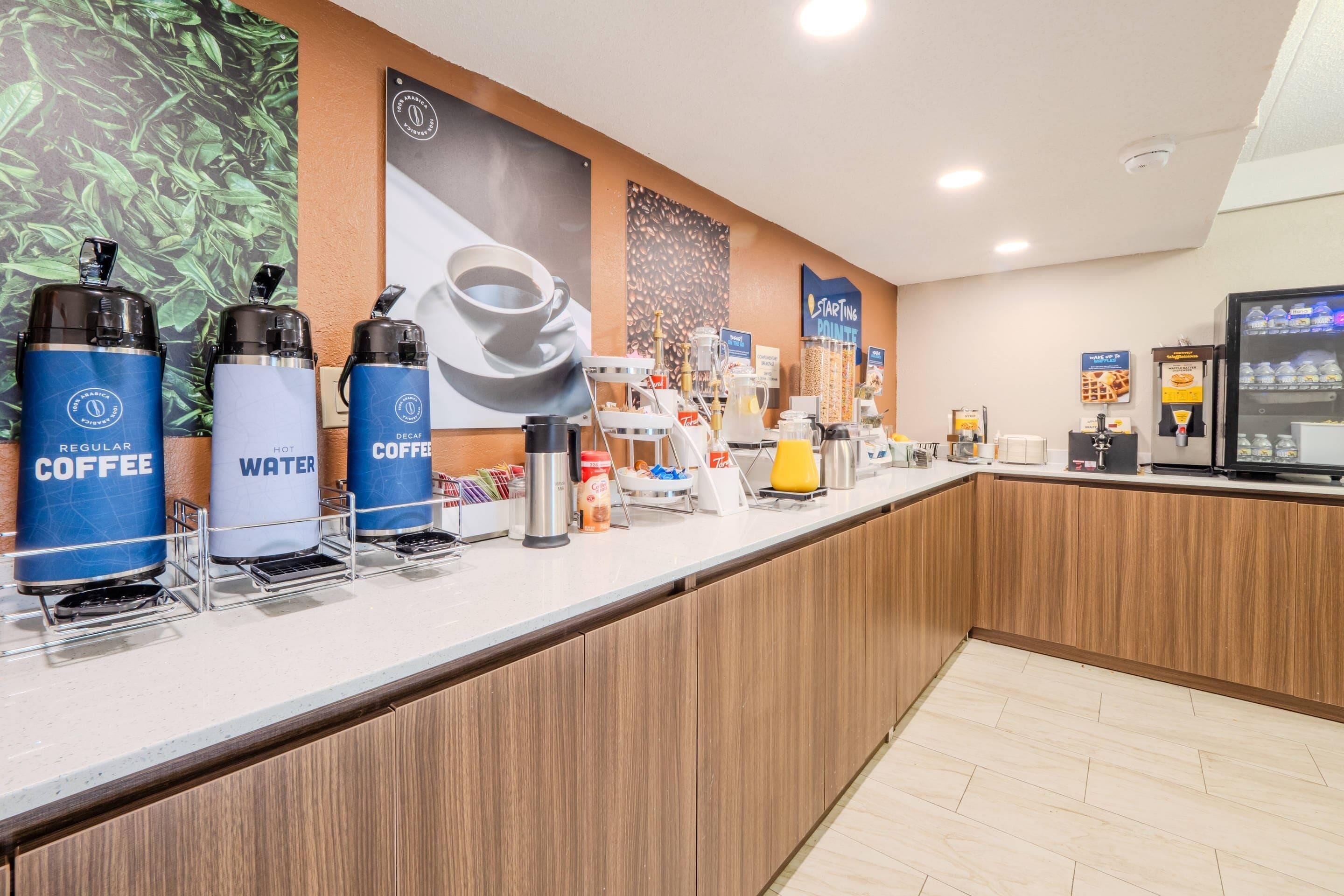 Una estación de café con dispensadores etiquetados como 'Regular Coffee' y 'Decaf Coffee', un refrigerador de agua y una máquina de café.