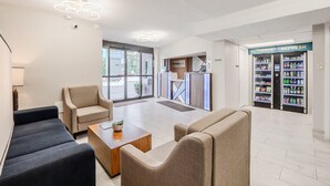 A modern reception area with seating, a reception desk, and a refrigerator labeled "RECHARGE REFRESH". - Clarion Pointe Winston – Salem Downtown (Winston-Salem)