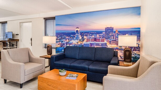 A modern hotel room with a cityscape view, a sofa, two armchairs, a coffee table, and a desk with a computer. - Clarion Pointe Winston – Salem Downtown (Winston-Salem)