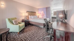 A hotel room with a bed, a desk, a chair, a lamp, and a wall with a cityscape painting. - Clarion Pointe Winston – Salem Downtown (Winston-Salem)