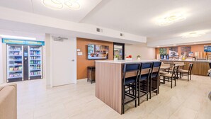 A modern hotel lobby with a reception desk, seating area, and vending machines. - Clarion Pointe Winston – Salem Downtown (Winston-Salem)