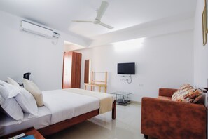 A modern hotel room with a bed, a sofa, a TV, and a ceiling fan. - Achates Corporate Services   (Bengaluru)