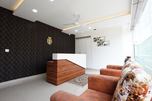 A modern reception area with a wooden reception desk, a patterned wall, and a large window. - Achates Corporate Services   (Bengaluru)