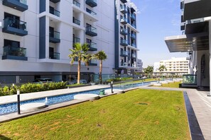 A modern building with multiple balconies, a swimming pool, and a well-maintained lawn. - Bloomfields Olivz Cozy STU International (Dubai)