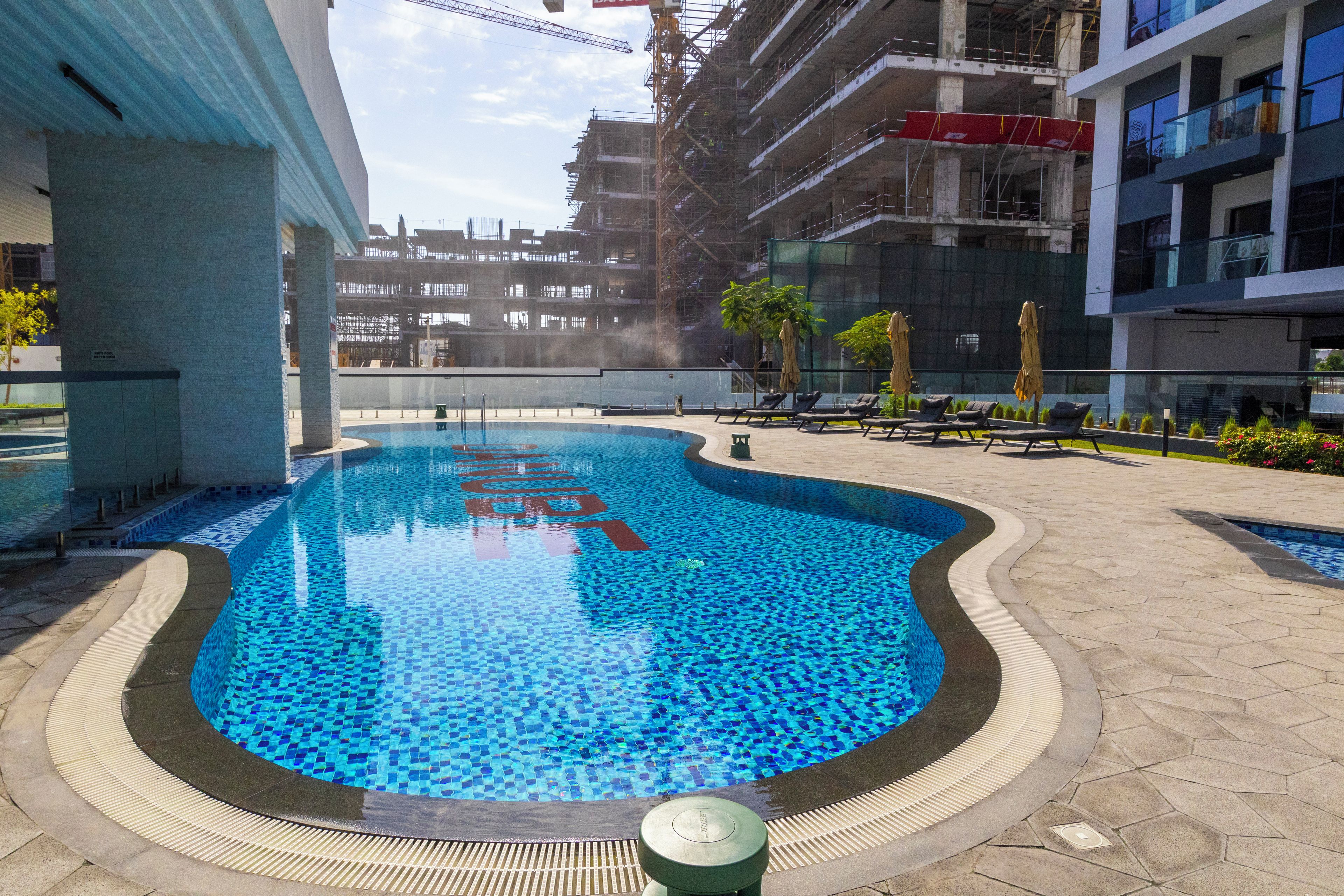 A swimming pool with a tiled edge, surrounded by a paved area with lounge chairs and umbrellas.