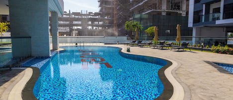 A swimming pool with a tiled edge, surrounded by a paved area with lounge chairs and umbrellas.