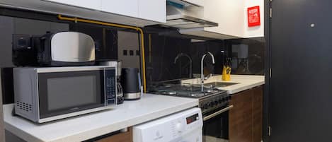 A compact kitchen with a microwave, coffee maker, sink, and a washing machine.