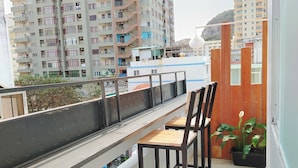 A balcony with a view of high-rise buildings, a railing, and two chairs. - Anh's House Modern Homestay 2 (Ho Chi Minh City)