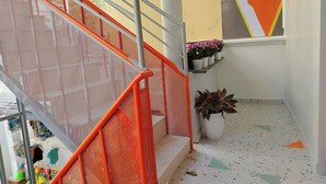 A staircase with orange railings and a perforated metal barrier. There are potted plants on the landing and a colorful wall mural. - Anh's House Modern Homestay 2 (Ho Chi Minh City)