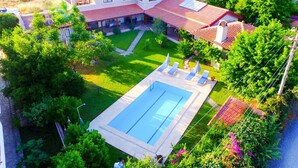 Una casa grande con piscina, rodeada de exuberante vegetación y un césped cuidado.