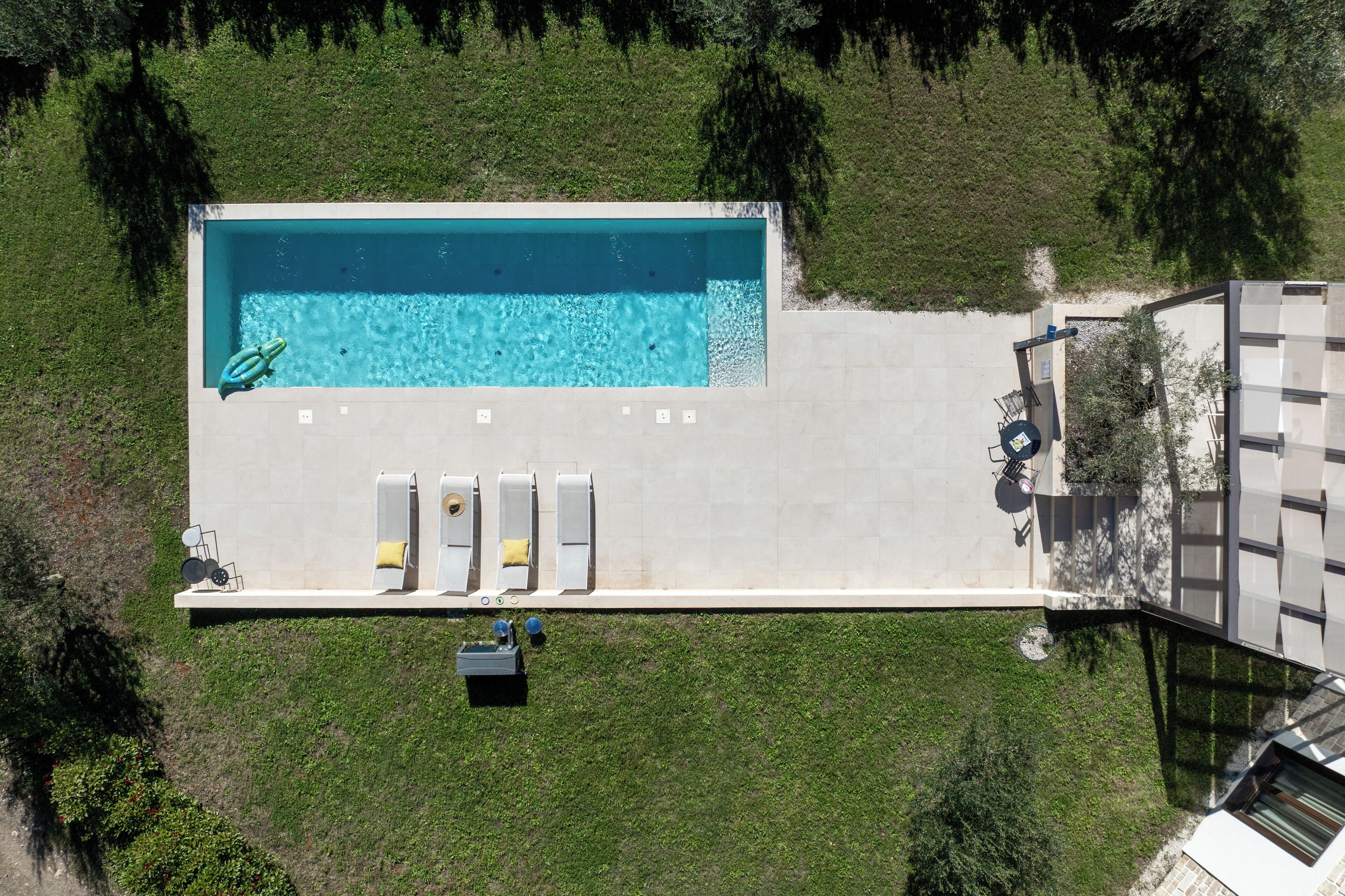 Vista aérea de una piscina rectangular con un flotador, una zona de descanso con tumbonas y una pequeña fuente de agua.