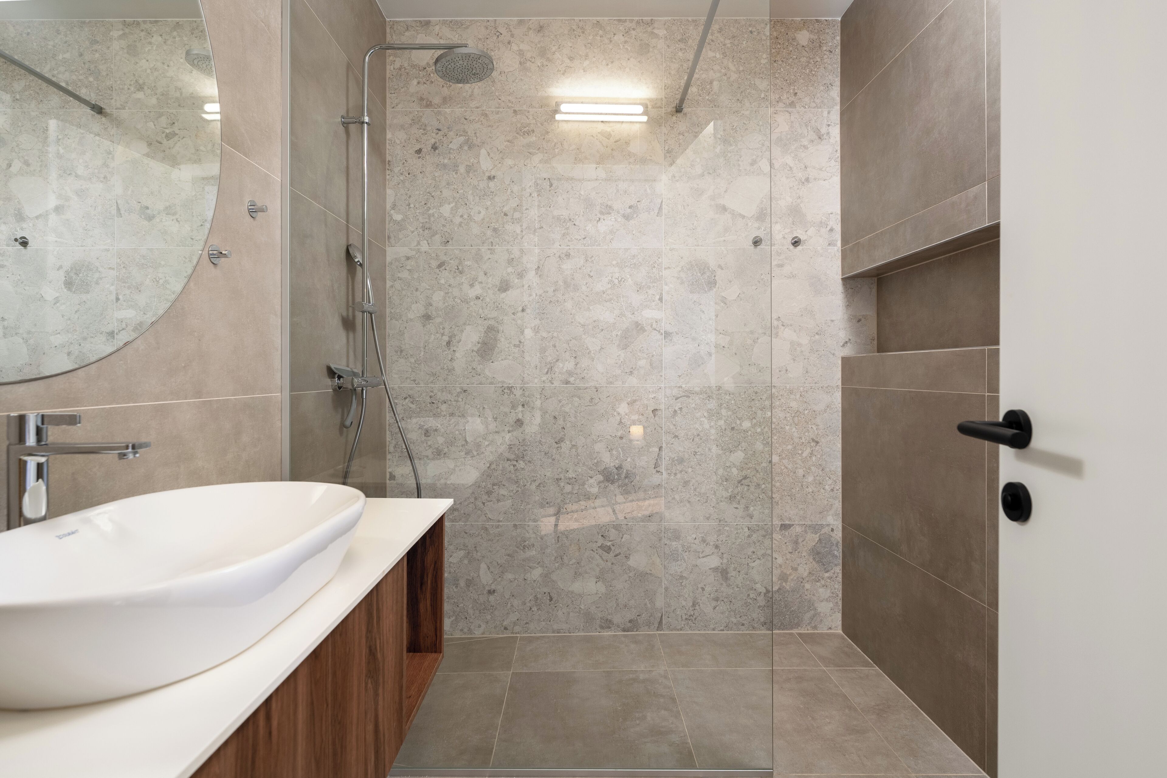 A modern bathroom with a large sink, a shower, and a mirror.