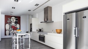 A modern kitchen with a stainless steel refrigerator, white cabinetry, and a dining area with clear chairs.